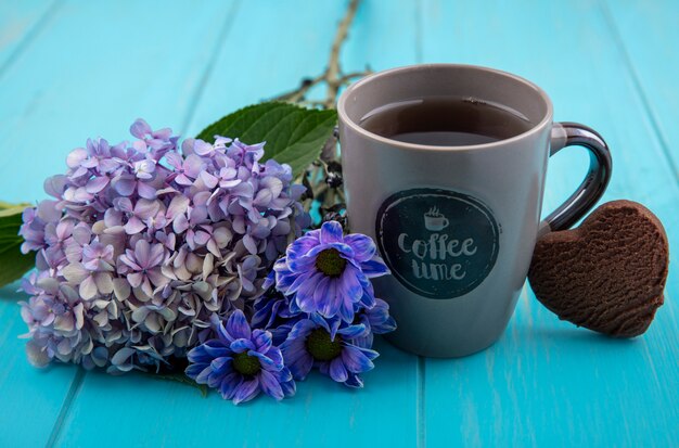 Side view of a cup of tea with lovely flowers isolated on a blue wooden background