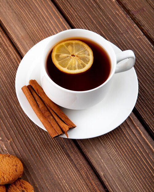 Side view cup of tea with a slice of lemon and cinnamon with cookies on a wooden background