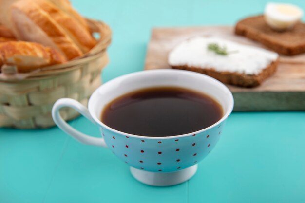 Side view of cup of tea with sliced baguette and rye bread slices smeared with cheese and egg with dill piece on blue background