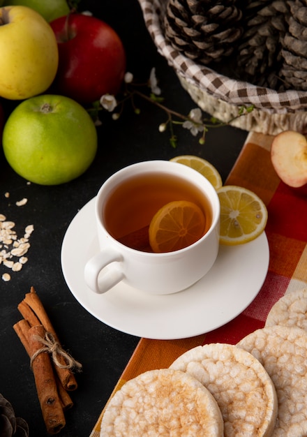 Side view cup of tea with sliced lemon and cinnamon with apples on the table