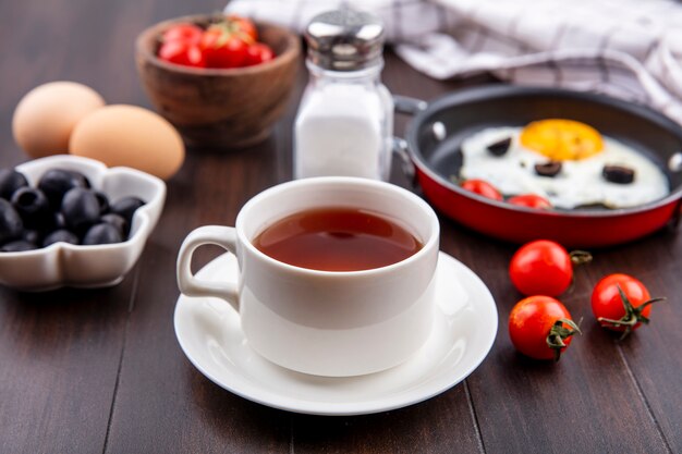 木の表面に紅茶とトマトの目玉焼き黒オリーブ塩のカップの側面図