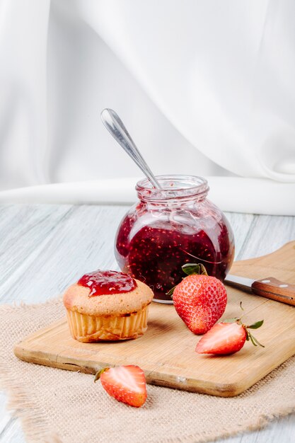 Side view cupcake with strawberry jam fresh strawberry knife and board on white background