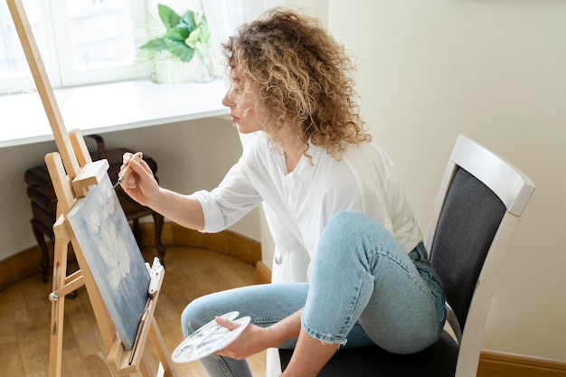 Side view of curly-haired woman painting at home