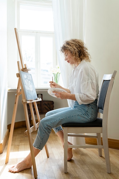 Free photo side view of curly-haired woman painting at home