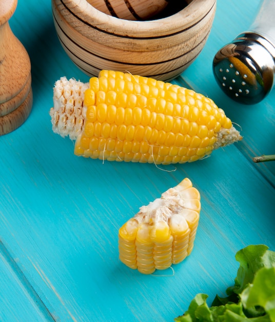 Side view of cut corn with lettuce salt on blue table