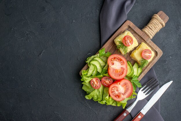 Side view of cut fresh tomatoes and cucumbers cheese on wooden board on the left side on black surface