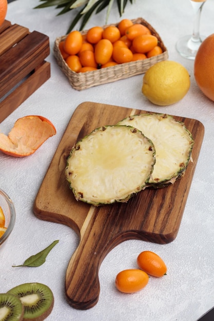 Side view of cut pineapple on cutting board with orange lemon kumquat with knife on white background