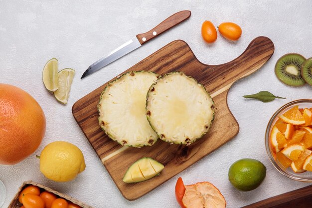 白い背景の上のナイフとオレンジレモンキンカンとまな板上のカットパイナップルの側面図