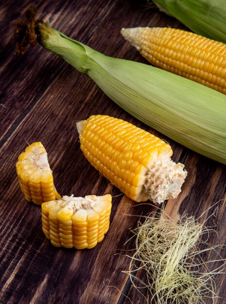 Side view of cut and whole corns with corn silk on wooden table