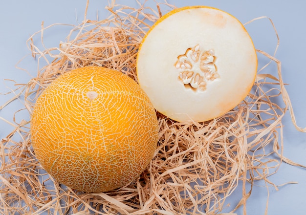 Foto gratuita vista laterale del taglio e interi meloni su paglia e sfondo grigio bluastro