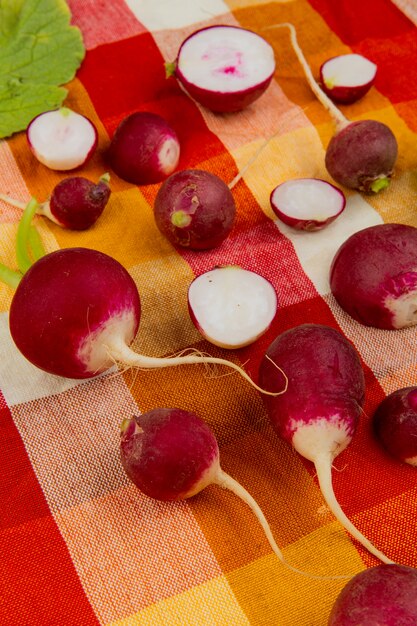 Side view of cut and whole radishes on plaid cloth background decorated with leaves