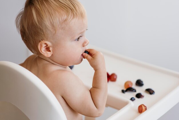 Side view cute baby in highchair choosing what fruit to eat