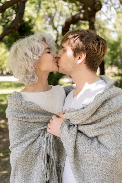 Side view of cute couple covered in blanket kissing outdoors