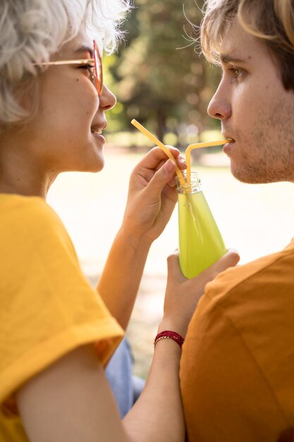 Side view of cute couple sharing juice with straws in the park