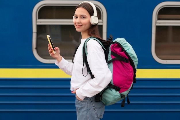 Ragazza carina vista laterale alla stazione ferroviaria tenendo il telefono cellulare