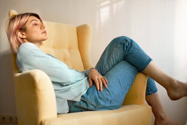 Side view of cute student girl lying barefooted in comfortable armchair relaxing.