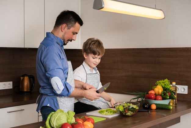 Free photo side view dad and son cutting vegetables