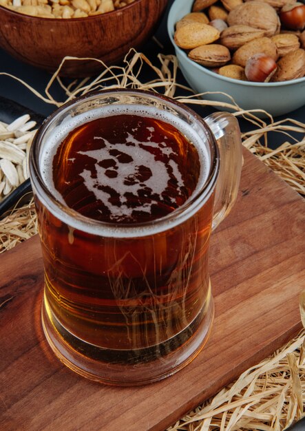 Вид сбоку темного пива в кружку на деревянной доске с соломой на деревенском