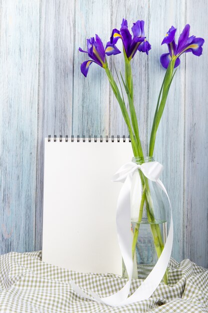 Side view of dark purple color iris flowers in a glass bottle with a sketchbook on wooden background