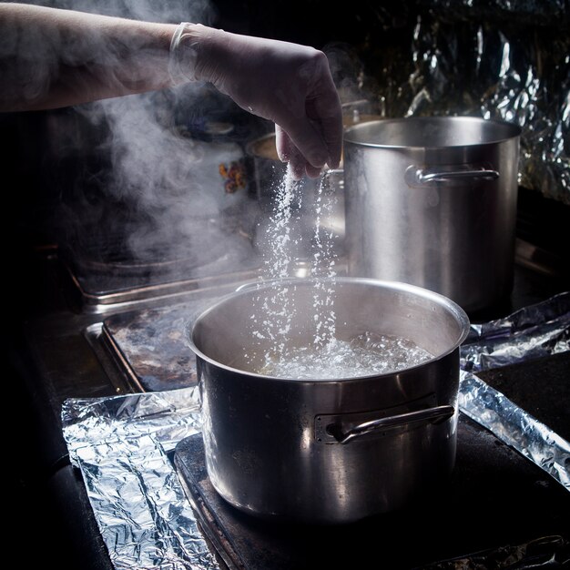 沸騰したお湯と塩とストーブで人間の手で深い鍋の側面図