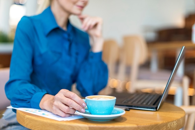 Side view of defocused older business woman having coffee while working on laptop