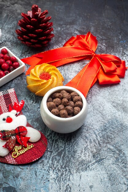 Side view of delicious biscuits and cornel on a white plate new year sock red conifer cone red ribbon on dark surface