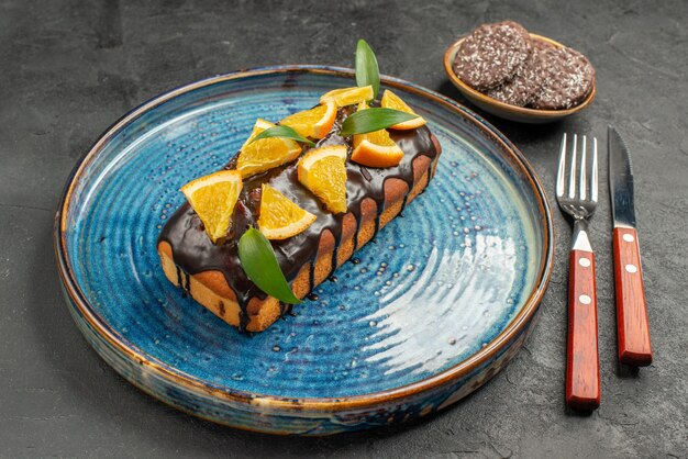 Side view of delicious cake and biscuits with fork and knife on black table