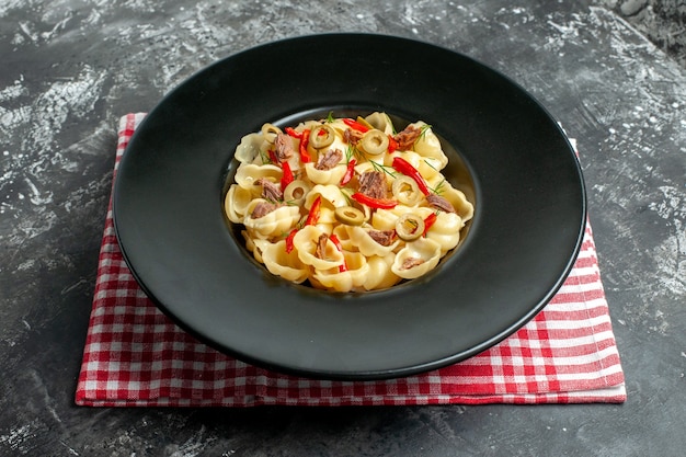 Side view of delicious conchiglie with vegetables and greens on a plate and knife on red stripped towel on gray background