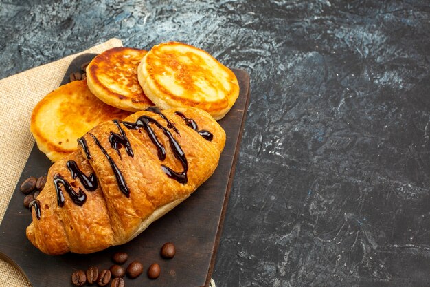 Side view of delicious croissant pancakes on wooden cutting board for beloved one on the right side on dark surface