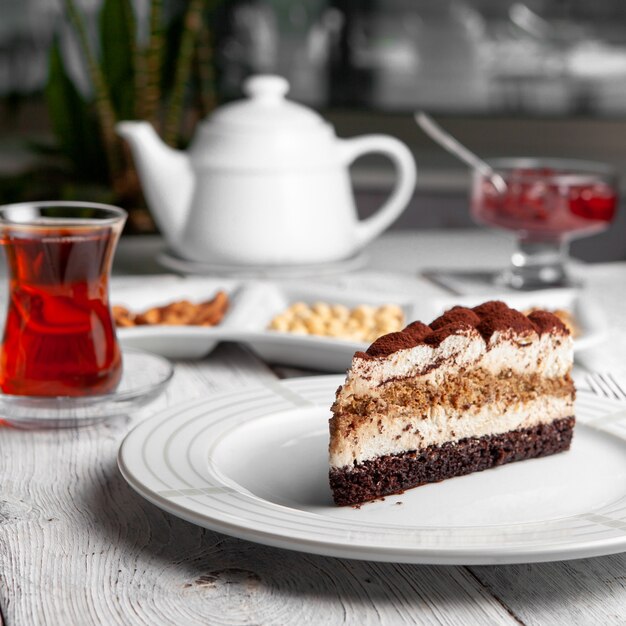 Side view delicious dessert in plate with tea, nuts, teapot, fruit jam on white wooden background.