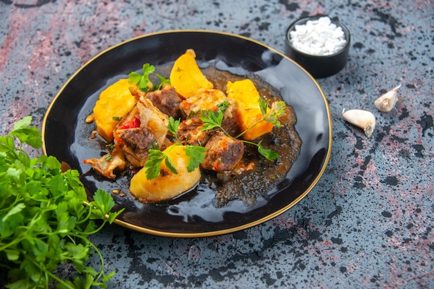 Side view of delicious dinner with meat potatoes served with green in a black plate and garlic salt on mix colors background