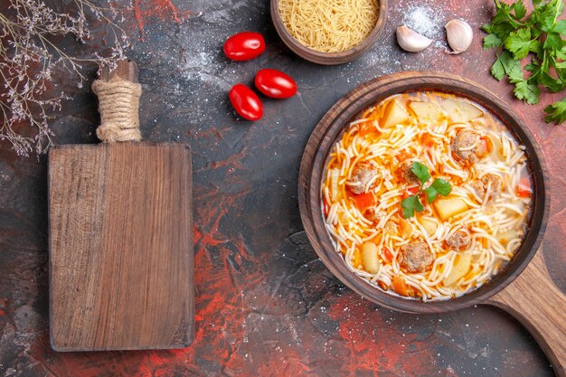 Side view of delicious noodle soup with chicken and wooden cutting board garlic tomatoes and greens on dark table