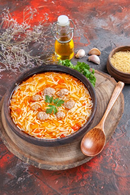 Side view of delicious noodle soup with chicken on wooden cutting board greens spoon oil bottle on dark background