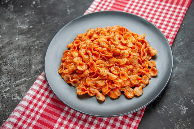 Side view of delicious pasta meal on a black plate for dinner on a red stripped towel on dark background