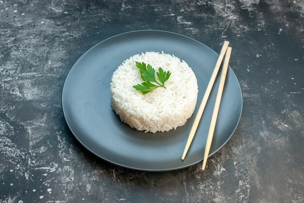 Вид сбоку вкусной рисовой еды, подаваемой с зеленью и палочками для еды на черной тарелке на темном фоне