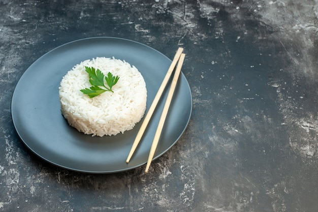 Side view of delicious rice meal served with green and chopsticks on a black plate on the right side on dark background