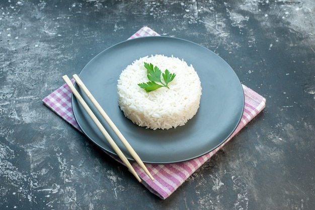 검은 배경에 보라색 벗겨진 수건에 검은 접시에 녹색 나무 젓가락으로 제공되는 맛있는 쌀 식사의 측면보기