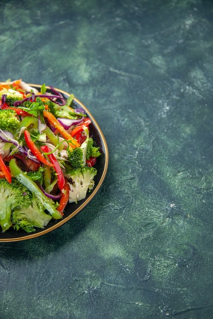 Free photo side view of delicious vegan salad in a plate with various fresh vegetables on the right side on dark background