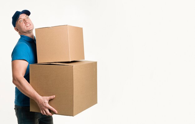 Вид сбоку доставщик держит тяжелые картонные коробки