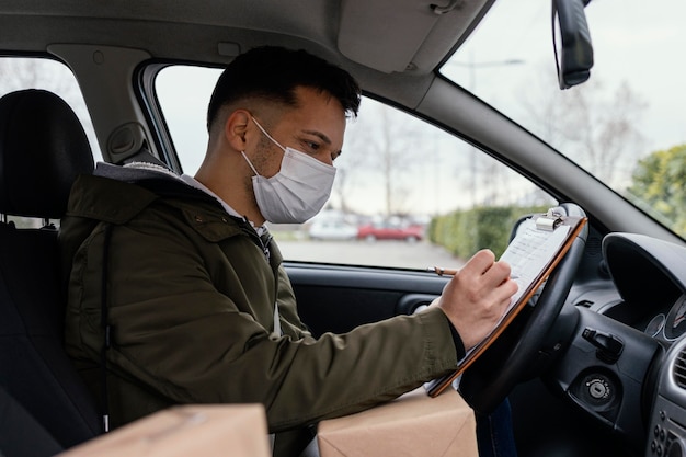 Free photo side view delivery man with mask in car