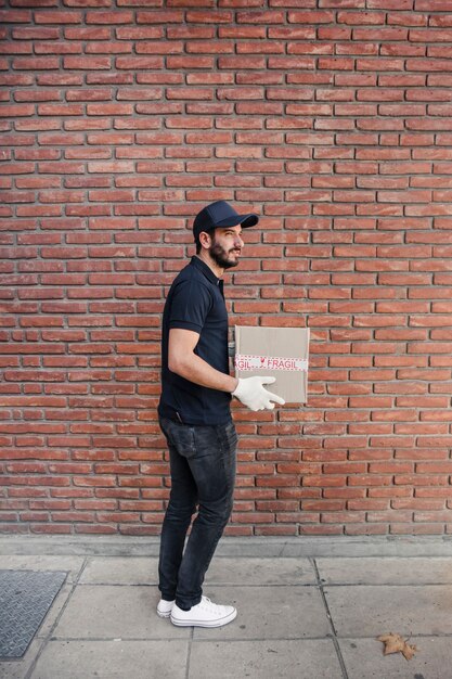 Side view of a delivery man with parcel in front of brickwall