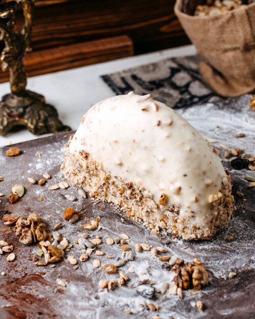 Side view of dessert covered with white chocolate and nuts on a wooden board