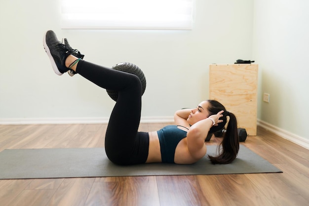 Side view of a determined young woman holding a slam ball with her legs and doing abdominal crunches to have flat abs