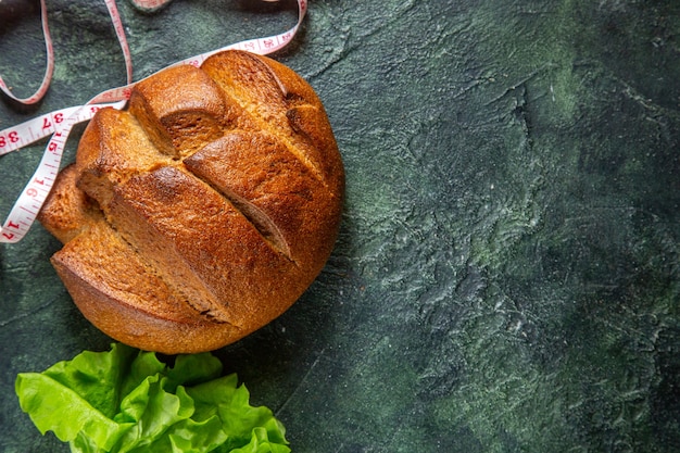 Side view of dietary black bread and meters green bundle on the right side on dark colors background