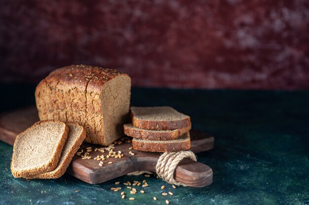 Side view of dietary black bread wheats on wooden cutting board on blue maroon mixed colors background