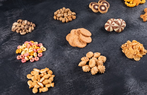 Side view of different kind of snacks as nuts, crackers and coockies on dark  horizontal