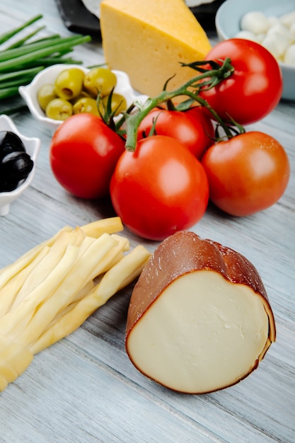Side view of different kinds of cheese with fresh tomatoes and pickled olives on grey wooden table