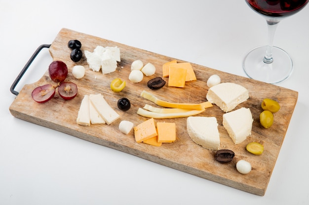 Side view of different kinds of cheese with grape pieces and olives on cutting board on white