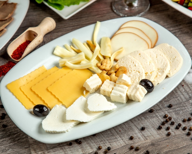 Side view of different types of cheese on a white plate on table