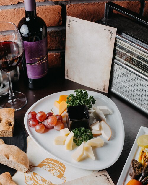 Side view of different types of cheese with grape on a white plate